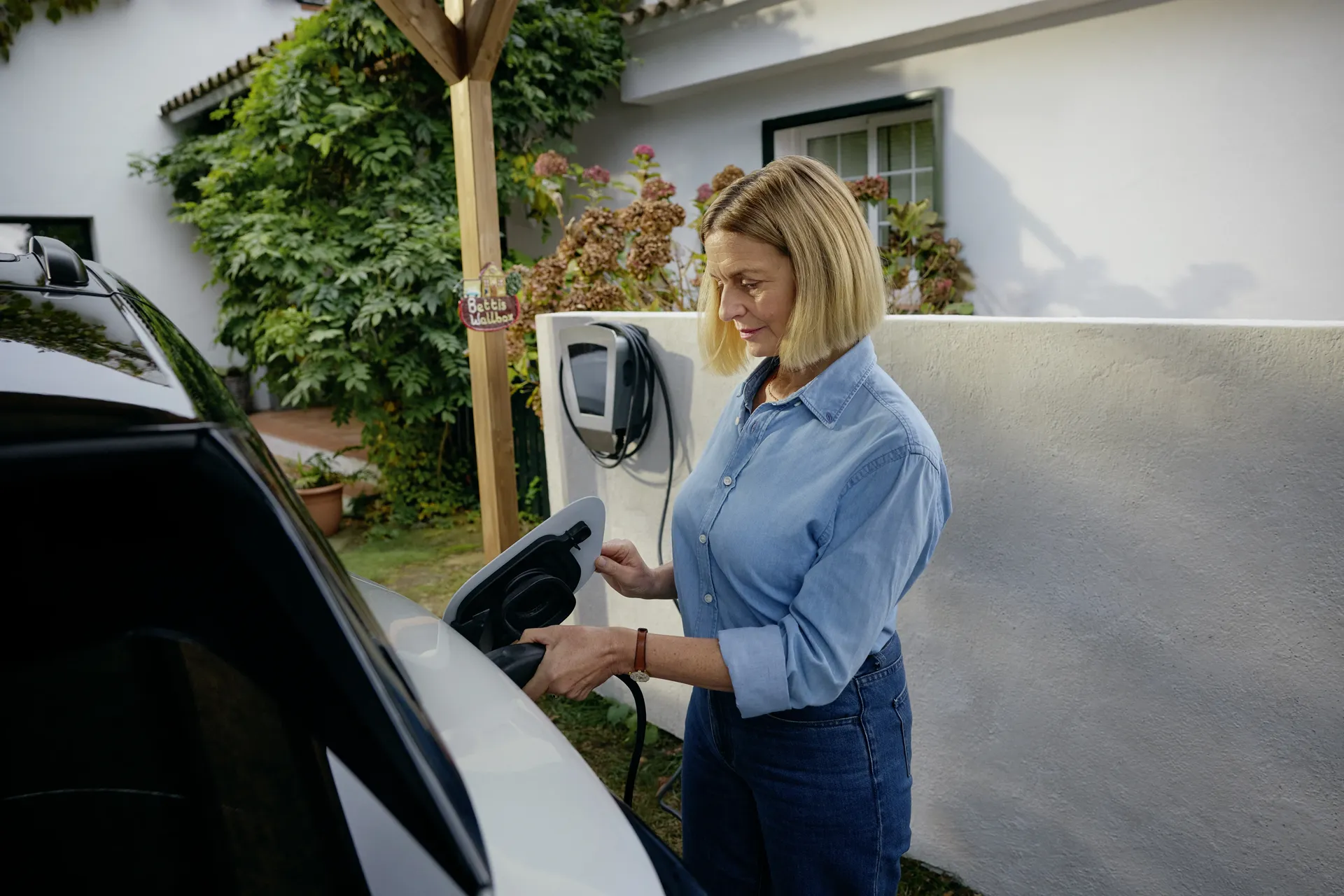 E-Mobilitäts-Kombi: Frau lädt ihr Elektroauto zu Hause an der Wallbox